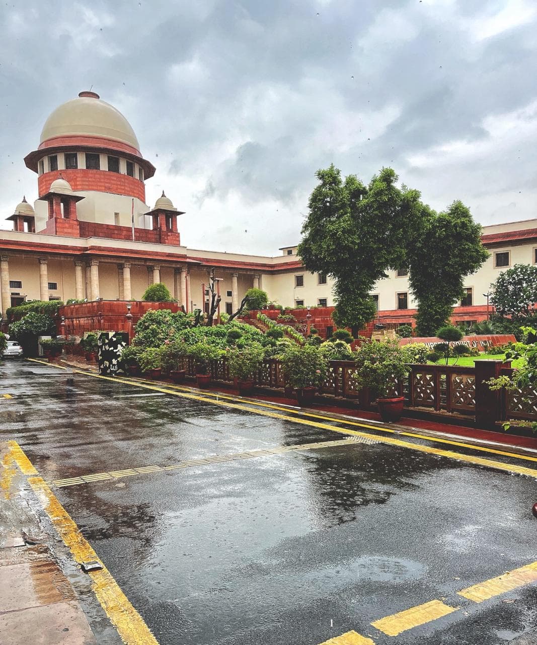Supreme Court of India building with its iconic dome under a rainy, overcast sky.