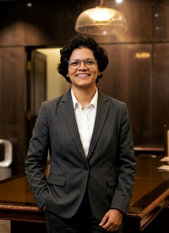 Smiling woman with glasses and short hair wearing a grey blazer in a professional office.